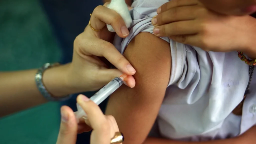 Close-up of a syringe injecting into a person’s upper arm while cotton is pressed on the skin.