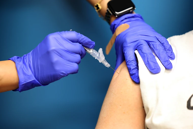 Close-up of syringe injection into upper arm with adhesive bandage visible.