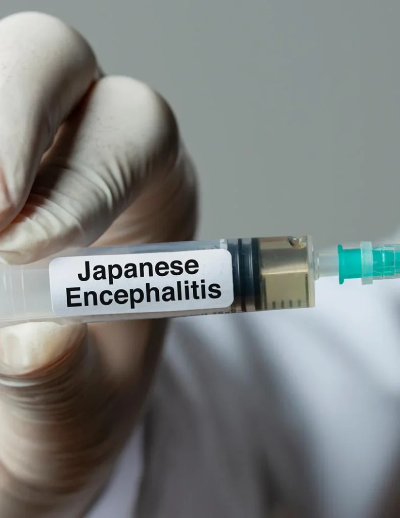 Gloved hand holding syringe labeled “Japanese Encephalitis” with clear liquid inside.