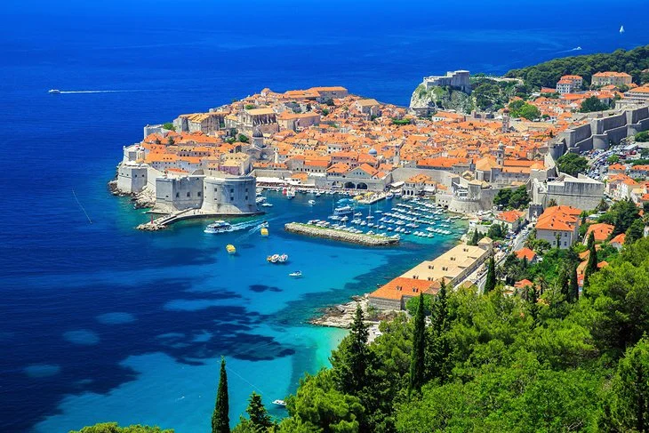 view of historic walled coastal city with orange rooftops, marina, and turquoise Adriatic waters.