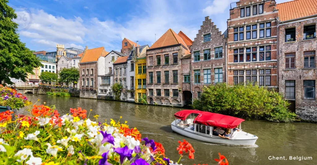 Scenic canal in Ghent, Belgium with historic Flemish buildings, boat carrying passengers, and colorful flowers in foreground.
