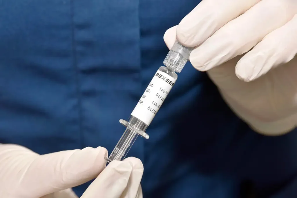 Close-up of gloved hands holding a syringe and vial labeled “BEXSERO” vaccine.