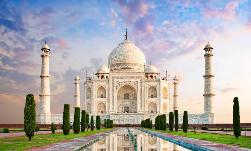 Taj Mahal in Agra, India with central dome, four minarets, reflecting pool, and colorful sunset sky.
