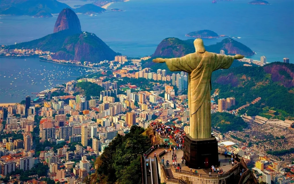 Christ the Redeemer statue atop Corcovado Mountain overlooking Rio de Janeiro cityscape, coastline, and Sugarloaf Mountain.